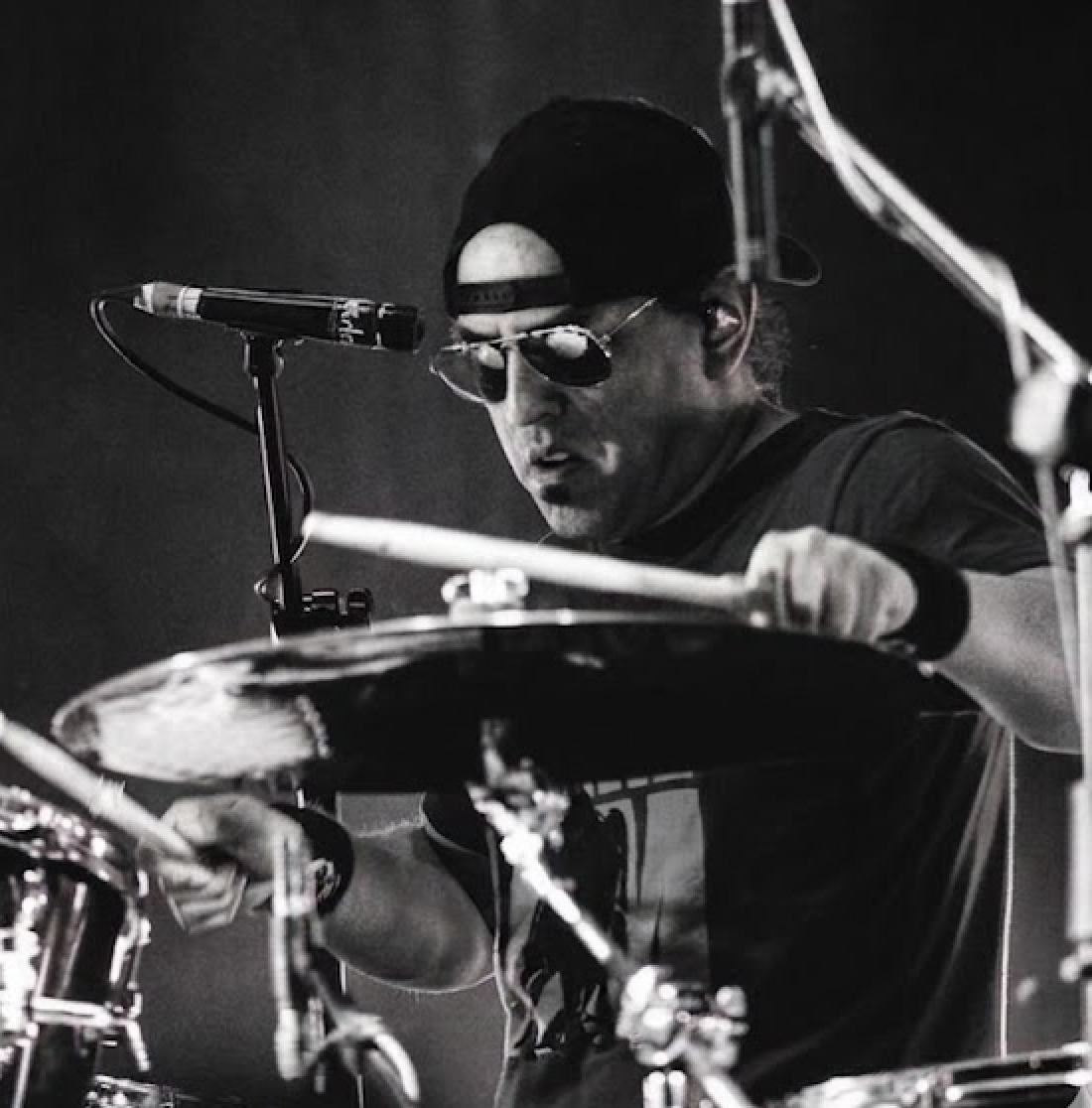 Retrato en blanco y negro de Hans Menacho tocando batería con lentes oscuros